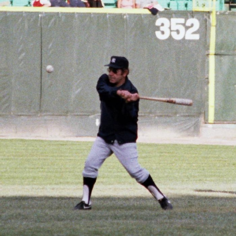 A baseball coach swings at a ball.
