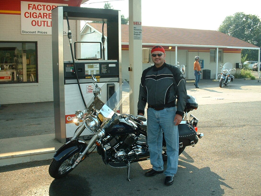 Man stands in front of a tank at a gas station with this motorcycle