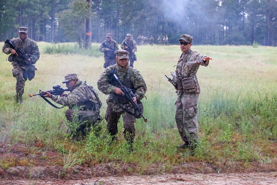 Soldiers stand next to one another holding weapons in a field.