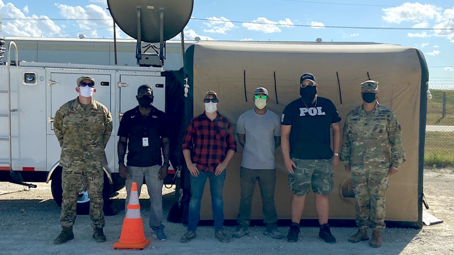 Six men stand in front of a mobile building with a satellite.