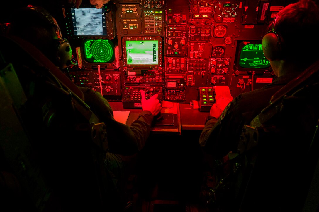 Two airmen sit in front of aircraft controls.