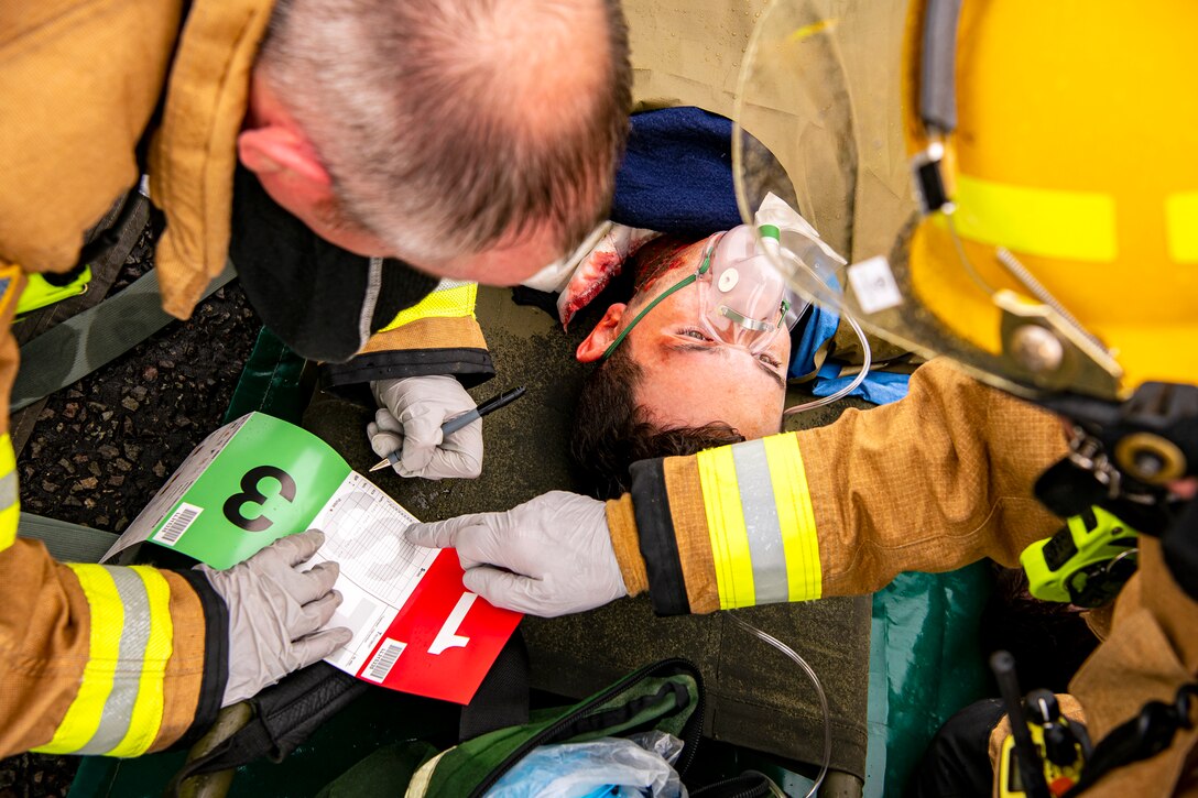 Firefighters from the 423rd Civil Engineer Squadron, right and left, transcribe vitals on a triage tag during an exercise at RAF Molesworth, England, Sept. 23, 2020. The exercise tested Airmen and firefighter’s preparedness and interoperability by responding to a simulated drone ordinance attack. (U.S. Air Force photo by Senior Airman Eugene Oliver)