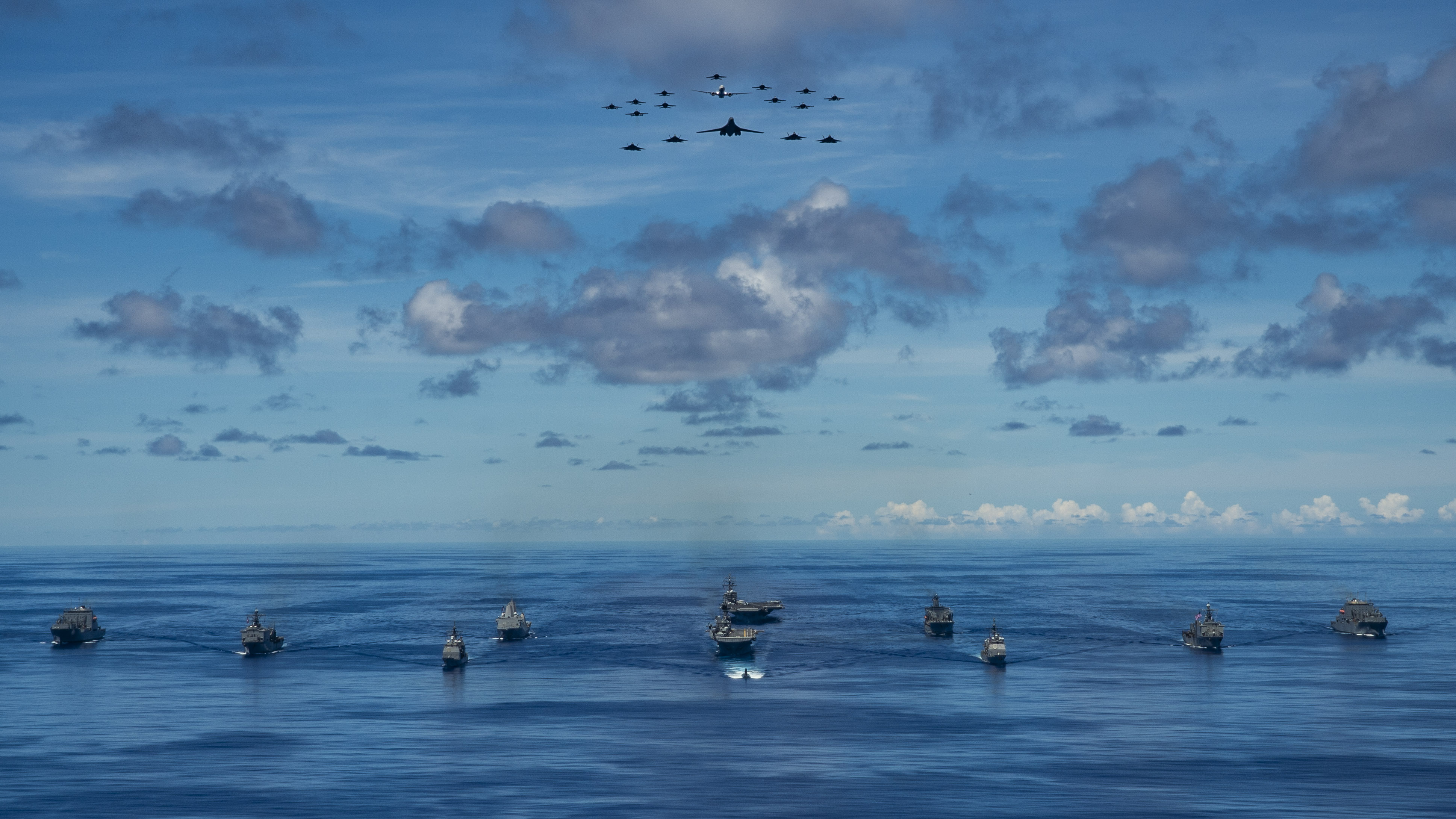 PHILIPPINE SEA (Sept. 25, 2020) From left, USNS Charles Drew (T-AKE 10), USS Comstock (LSD 45), USS Shiloh (CG 67), USS New Orleans (LPD 18), USS Chicago (SSN 721), USS America (LHA 6), USS Ronald Reagan (CVN 76), USNS John Ericsson (T-AO 194), USS Antietam (CG 54), USS Germantown (LSD 42), and USNS Sacagawea (T-AKE 2) steam in formation while E/A-18G Growlers and FA-18E Super Hornets from Carrier Air Wing (CVW) 5, a P-8 Poseidon from Commander Task Force 72, and U.S. Air Force F-22 Raptors and a B-1B Bomber fly over the formation in support of Valiant Shield 2020. Valiant Shield is a U.S. only, biennial field training exercise (FTX) with a focus on integration of joint training in a blue-water environment among U.S. forces. This training enables real-world proficiency in sustaining joint forces through detecting, locating, tracking and engaging units at sea, in the air, on land and in cyberspace in response to a range of mission areas. (U.S. Navy photo by Mass Communication Specialist 2nd Class Codie Soule)