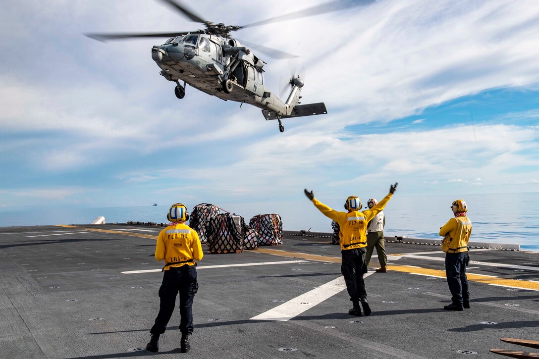 Sailors signal a helicopter while standing on a ship.