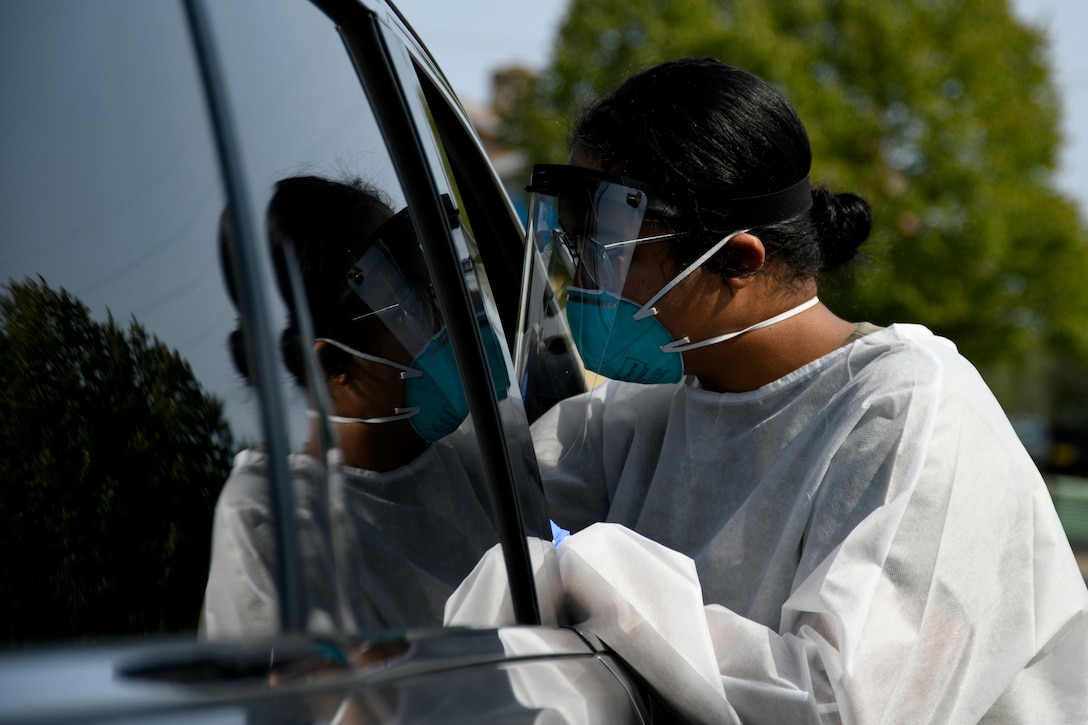 A service member in protective gear looks into a car window.