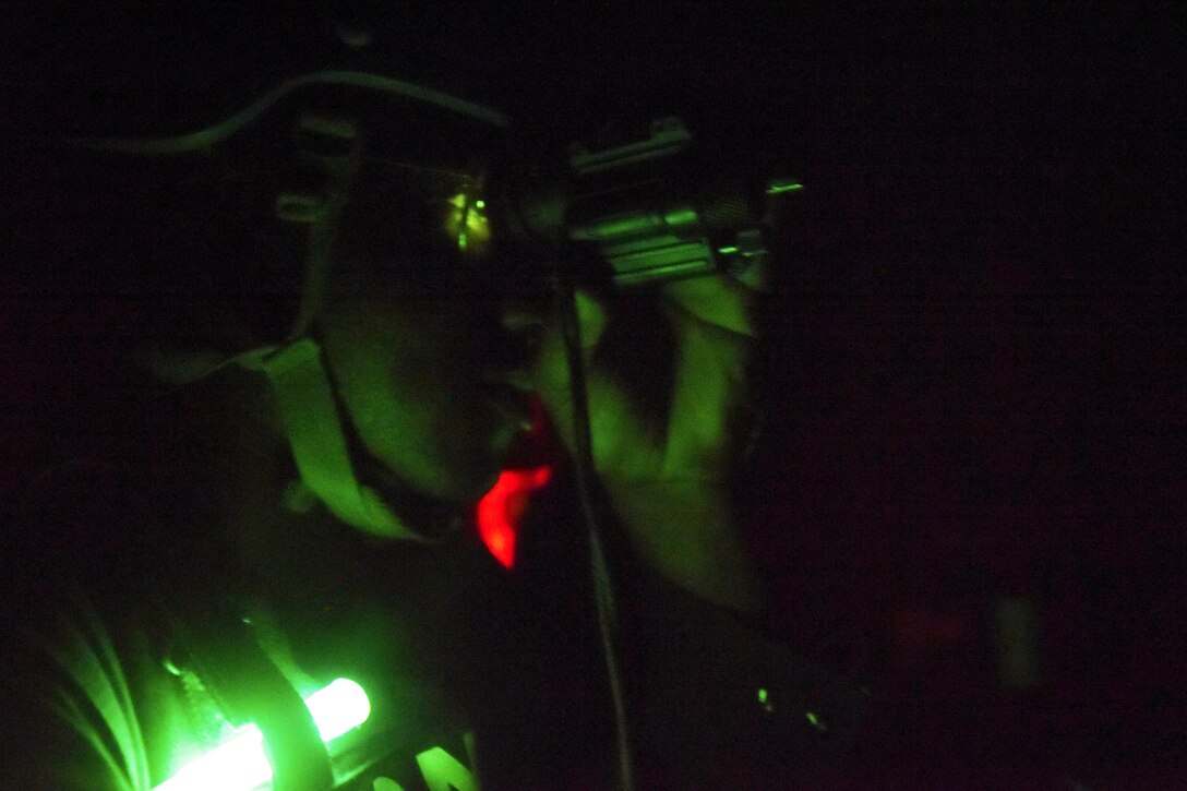 A sailors wears protective gear illuminated by green light.