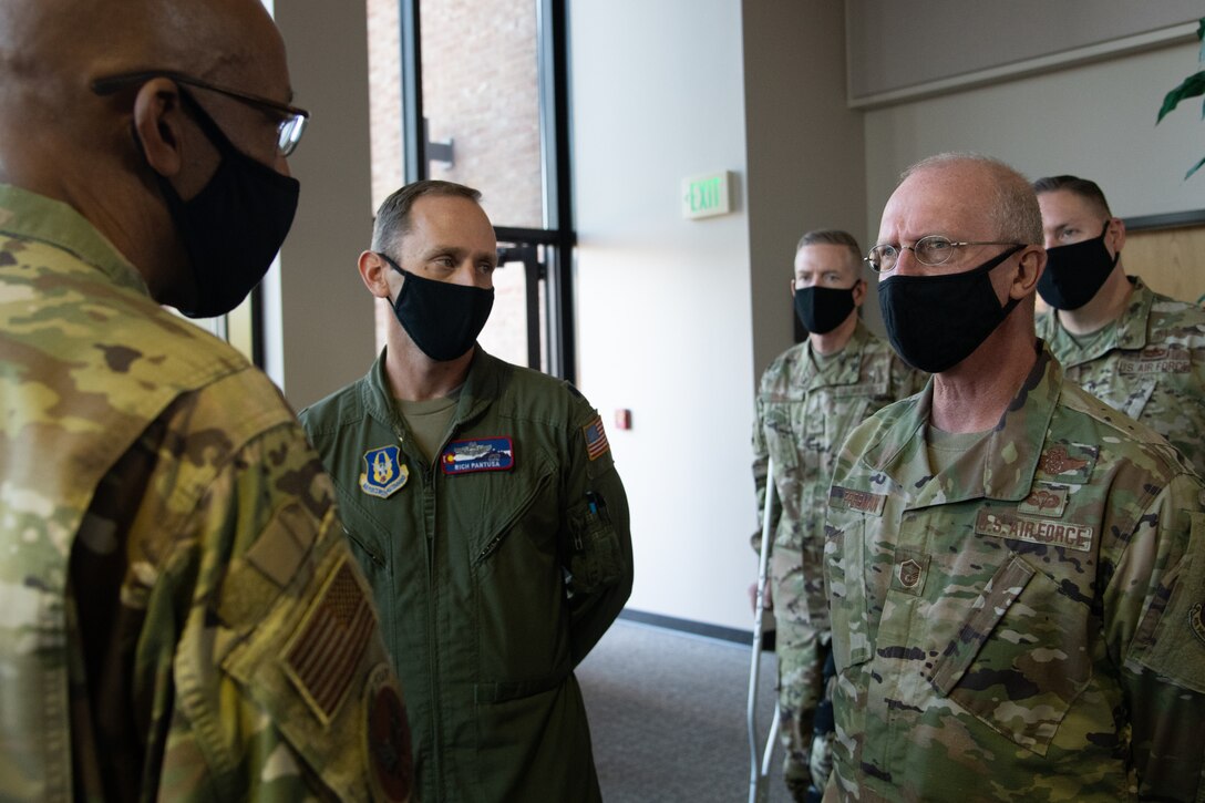 Two men wearing black masks converse, while three men wearing black masks observe the conversation.