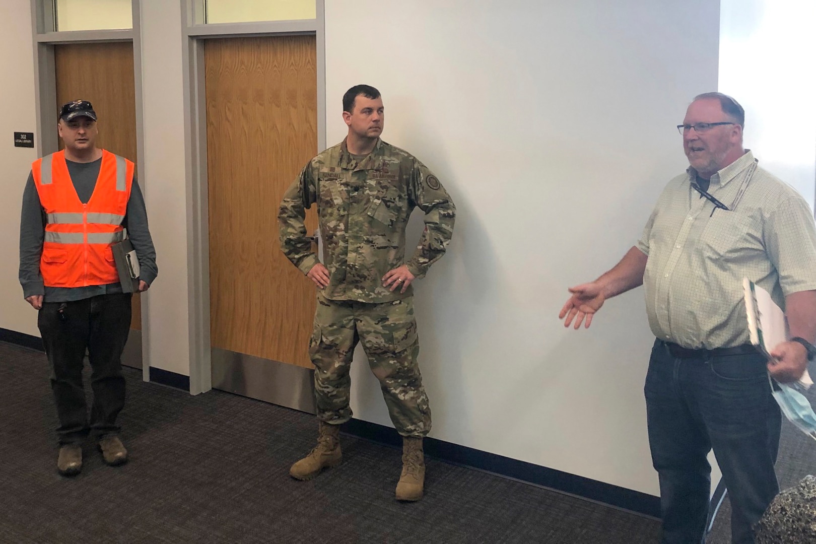 a service member in the center of the frame speaks with two civilian employees