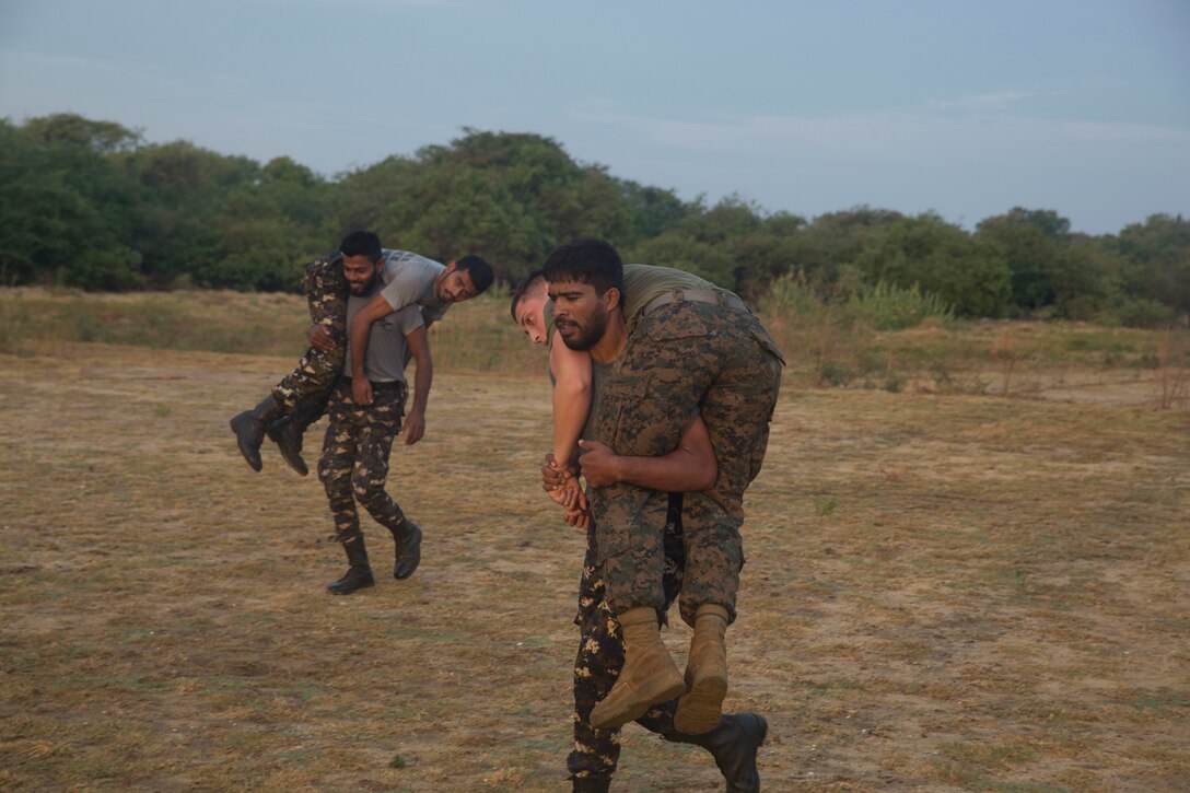 Two military personnel each carry a person over their shoulders.