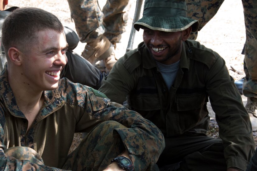 Two military personnel sit on the ground near each other.