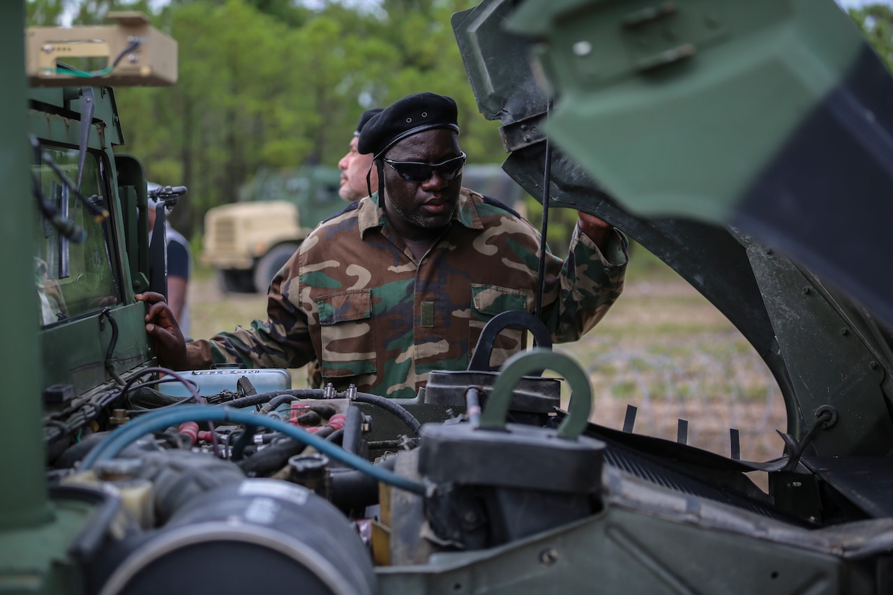 A man in a military uniform checks under the hood of a military vehicle.