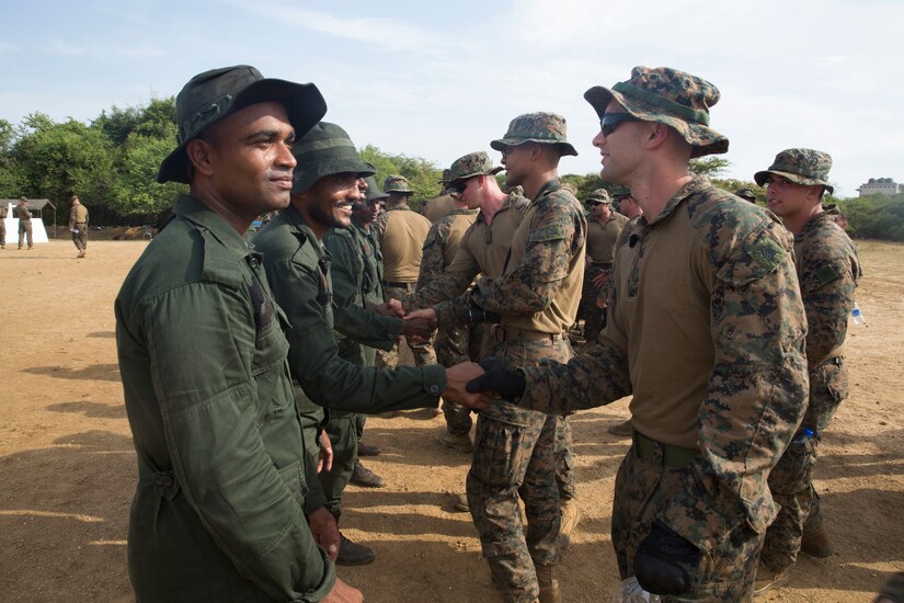 Military personnel in different uniforms shake hands with one another.