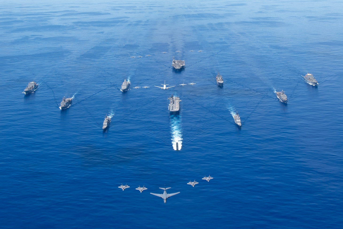 PHILIPPINE SEA (Sept. 25, 2020) From left, USNS Charles Drew (T-AKE 10), USS Comstock (LSD 45), USS Shiloh (CG 67), USS New Orleans (LPD 18), USS Chicago (SSN 721), USS America (LHA 6), USS Ronald Reagan (CVN 76), USNS John Ericsson (T-AO 194), USS Antietam (CG 54), USS Germantown (LSD 42), and USNS Sacagawea (T-AKE 2) steam in formation while E/A-18G Growlers and FA-18E Super Hornets from Carrier Air Wing (CVW) 5, a P-8 Poseidon from Commander Task Force 72,  and U.S. Air Force F-22 Raptors and  a B-1B Bomber fly over the formation in support of Valiant Shield 2020. Valiant Shield is a U.S. only, biennial field training exercise (FTX) with a focus on integration of joint training in a blue-water environment among U.S. forces. This training enables real-world proficiency in sustaining joint forces through detecting, locating, tracking and engaging units at sea, in the air, on land and in cyberspace in response to a range of mission areas. (U.S. Navy photo by Mass Communication Specialist 3rd Class Jason Tarleton)