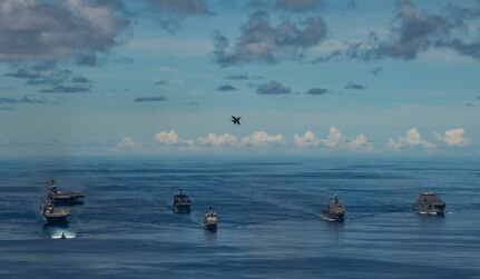 PHILIPPINE SEA (Sept. 25, 2020) USS Chicago (SSN 721), front, USS America (LHA 6), USS Ronald Reagan (CVN 76), USNS John Ericsson (T-AO 194) and USS Antietam (CG 54) steam in formation while an F/A-18E Super Hornet, attached to the Eagles of Strike Fighter Squadron (VFA) 115, flies over the formation in support of Valiant Shield 2020. Valiant Shield is a U.S. only, biennial field training exercise (FTX) with a focus on integration of joint training in a blue-water environment among U.S. forces. This training enables real-world proficiency in sustaining joint forces through detecting, locating, tracking and engaging units at sea, in the air, on land and in cyberspace in response to a range of mission areas. (U.S. Navy photo by Mass Communication Specialist 2nd Class Erica Bechard)