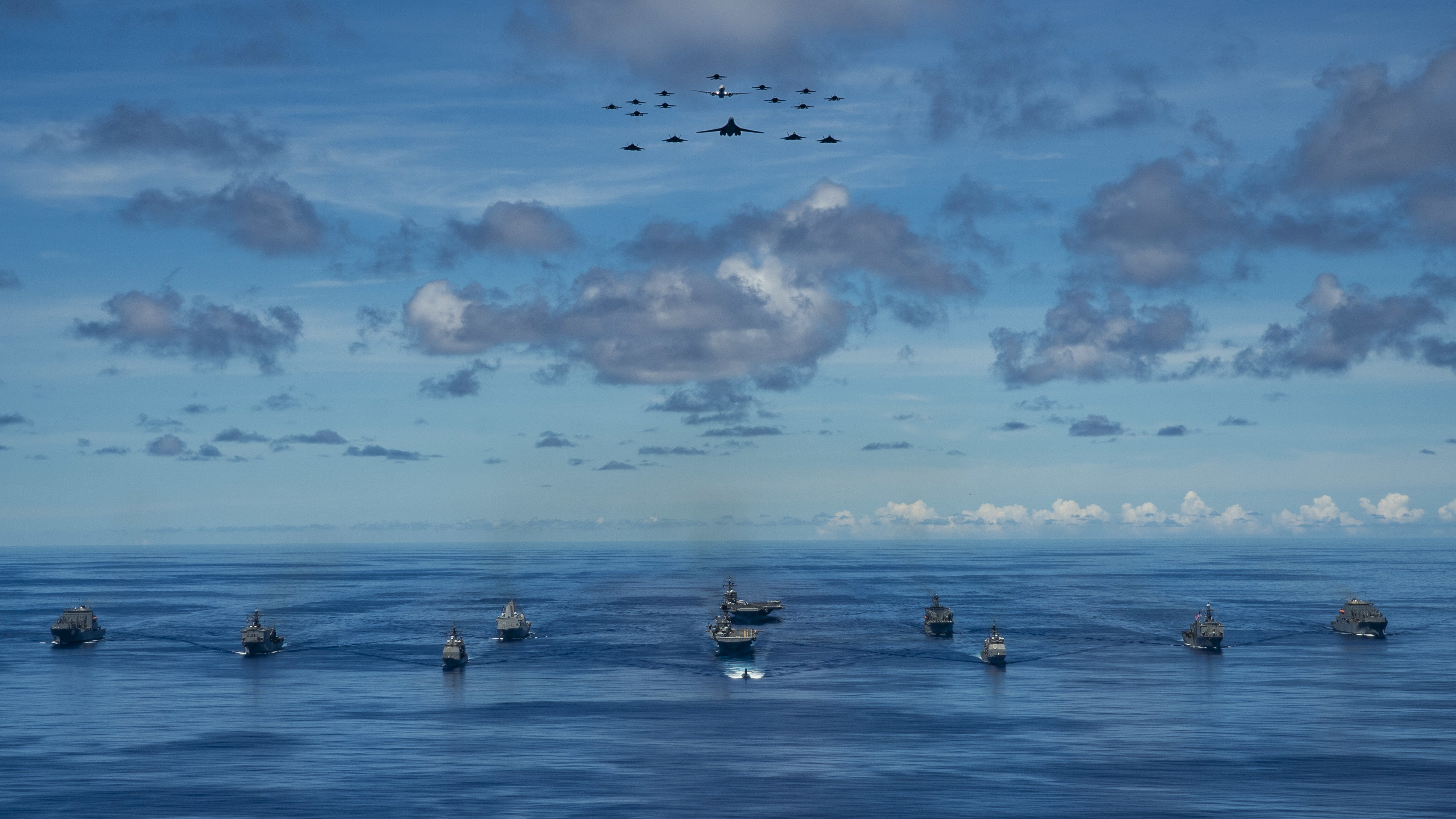 Ships participating in Valiant Shield 2020 steam in formation while E/A-18G Growlers and FA-18E Super Hornets from Carrier Air Wing (CVW) 5, a P-8 Poseidon assigned to Commander Task Force 72, and U.S. Air Force F-22 Raptors and a B-1B Bomber fly over the formation.