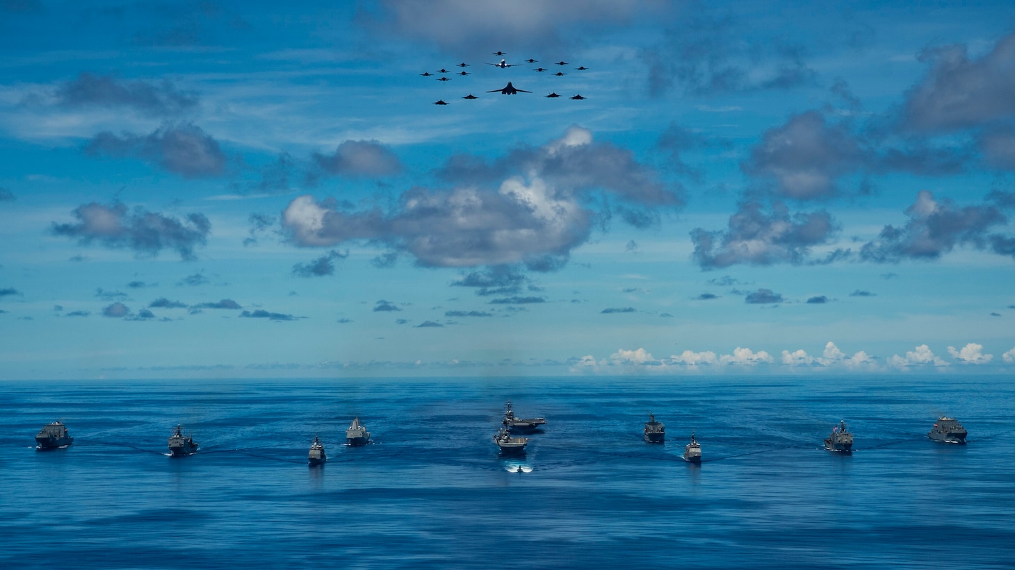 Ships participating in Valiant Shield 2020 steam in formation while E/A-18G Growlers and FA-18E Super Hornets from Carrier Air Wing (CVW) 5, a P-8 Poseidon assigned to Commander Task Force 72, and U.S. Air Force F-22 Raptors and a B-1B Bomber fly over the formation.