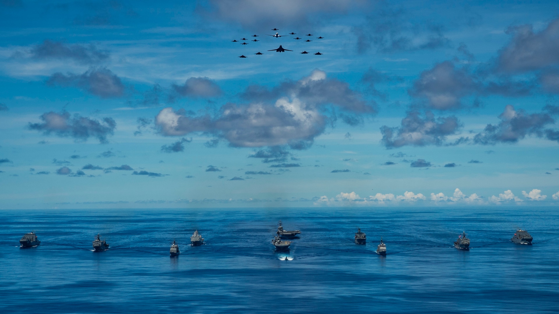 IMAGE: PHILIPPINE SEA (Sept. 25, 2020) - USNS Charles Drew (T-AKE 10), USS Comstock (LSD 45), USS Shiloh (CG 67), USS New Orleans (LPD 18), USS Chicago (SSN 721), USS America (LHA 6), USS Ronald Reagan (CVN 76), USNS John Ericsson (T-AO 194), USS Antietam (CG 54), USS Germantown (LSD 42) and USNS Sacagawea (T-AKE 2) steam in formation while E/A-18G Growlers, FA-18E Super Hornets, a P-8 Poseidon, U.S. Air Force F-22 Raptors and a B-1B Bomber fly over the formation in support of Valiant Shield 2020. Meanwhile, a team of Naval Surface Warfare Center Dahlgren Division (NSWCDD) scientists and engineers worked from two locations – Dahlgren, Va., and Honolulu, Hawaii – to ensure the success of this year’s Valiant Shield exercise. “Our biggest strategic accomplishment was supporting live forces, both afloat and at terrestrial sites, using a combined in-person and local operations team,” said Joseph Pack, NSWCDD deputy director for expeditionary warfare, regarding Dahlgren’s impact on the exercise that focuses on the integration of joint training in a blue-water environment among U.S. forces.  (U.S. Navy photo by Mass Communication Specialist 2nd Class Codie L. Soule)