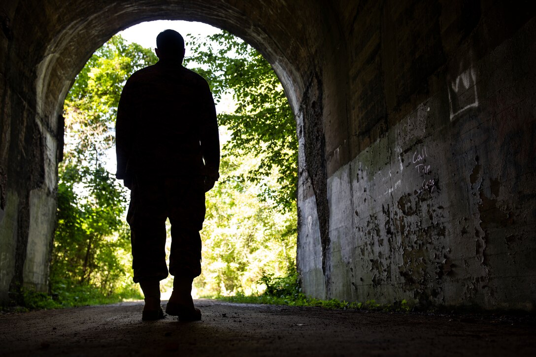 The silhouette of a person walking out of a dark tunnel and into the light.