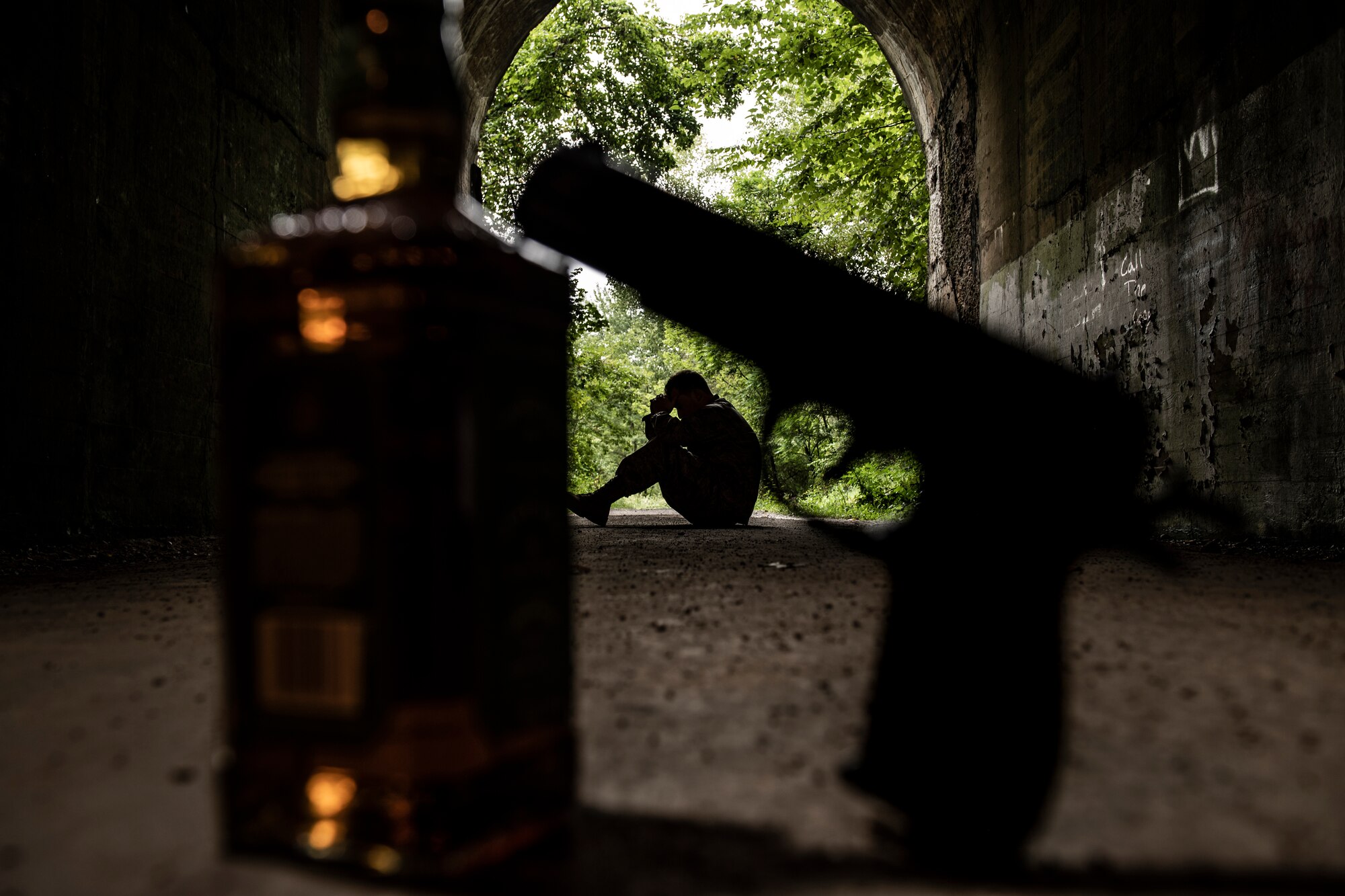 The silhouette of a person at the end of a tunnel framed by a bottle of alcohol and the silhouette of a pistol.