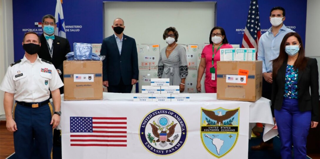 People in mask pose for a photo around a table with donated personal protection equipment.
