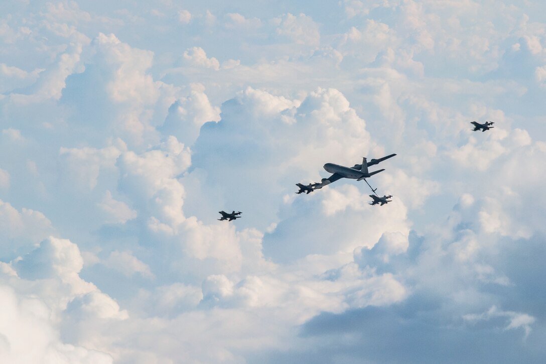 An aircraft refuels another aircraft as others fly nearby.