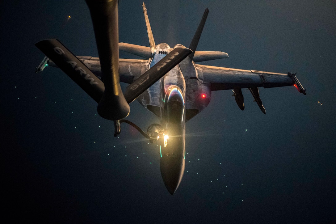 An aircraft refuels with another aircraft illuminated by green light.