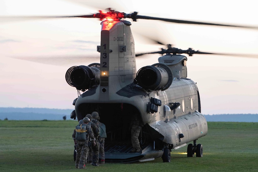 Three service members prepare to board a helicopter.