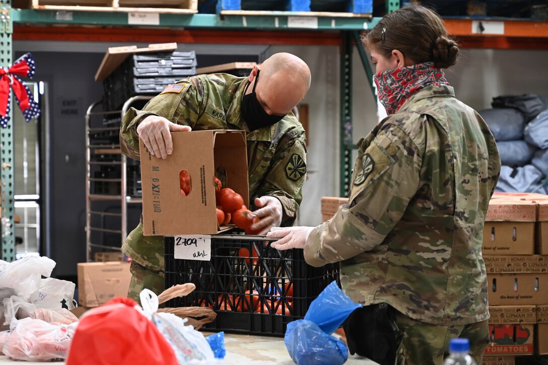 Two service members package vegetables and other groceries at a food bank.