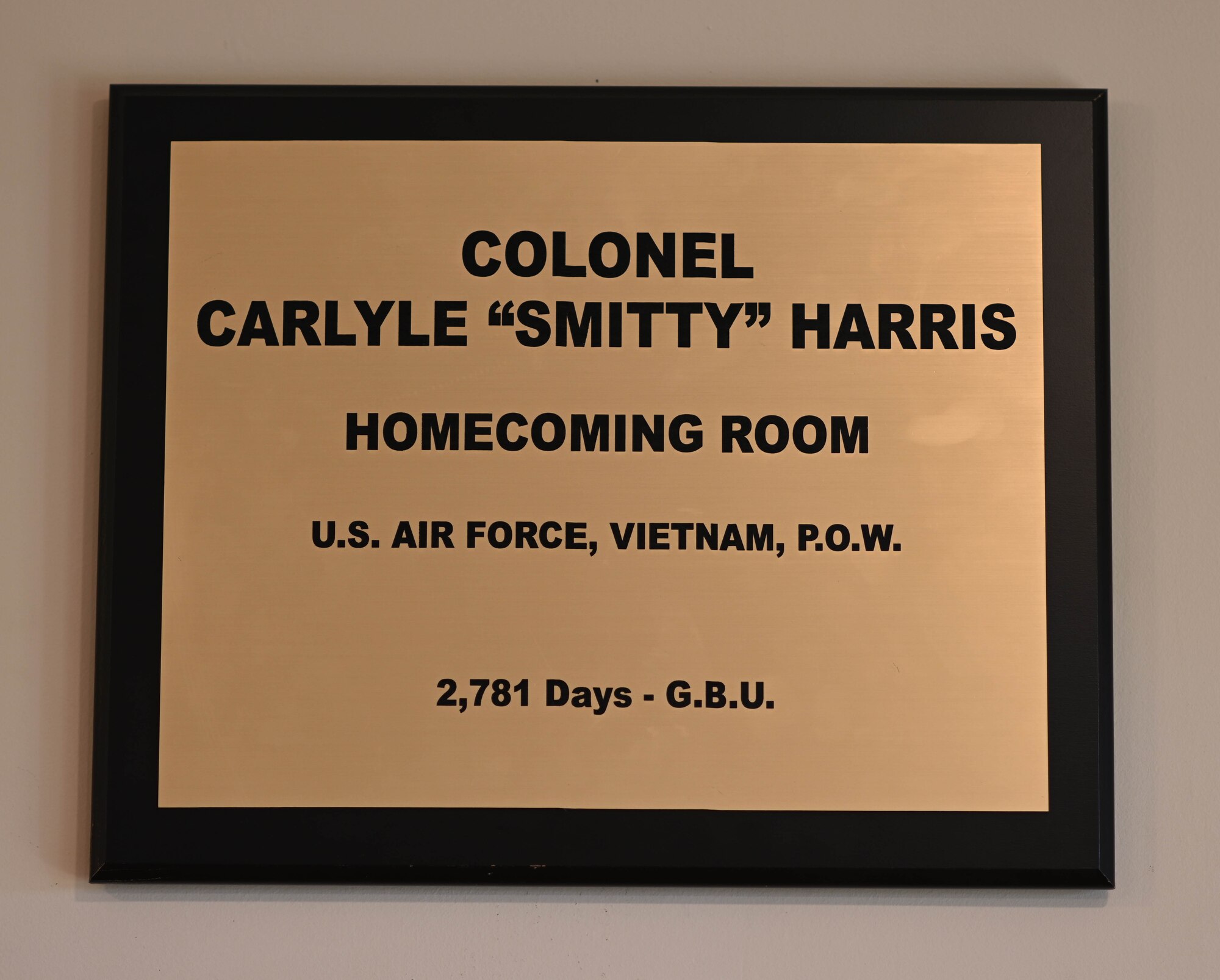 A plaque with Ret. Col. Carlyle “Smitty” Harris’ name is placed above a room dedicated to Harris. Harris and other POWs would use a tap code to tap the acronym “G.B.U.”, which stands for “God Bless You”. (U.S. Air Force photo by Airman 1st Class Davis Donaldson)