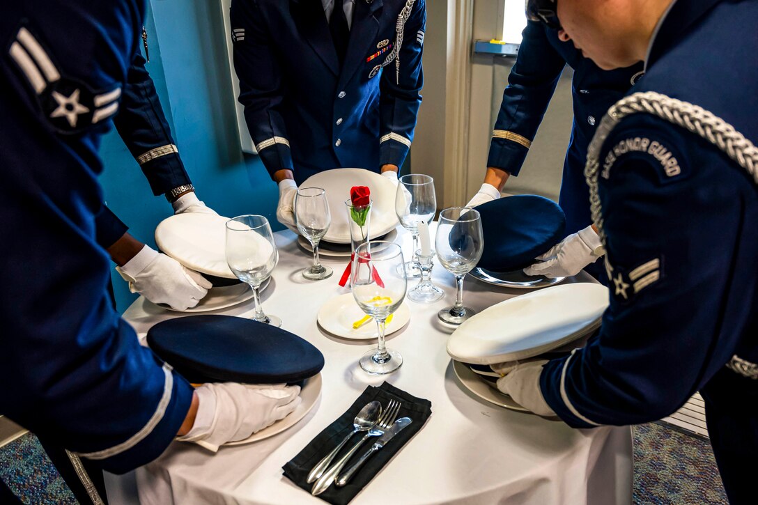 Airmen place covers on a circular table with a white tablecloth.