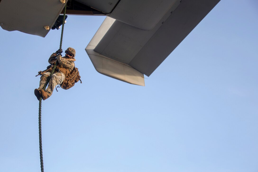 A service member rappels from an aircraft.
