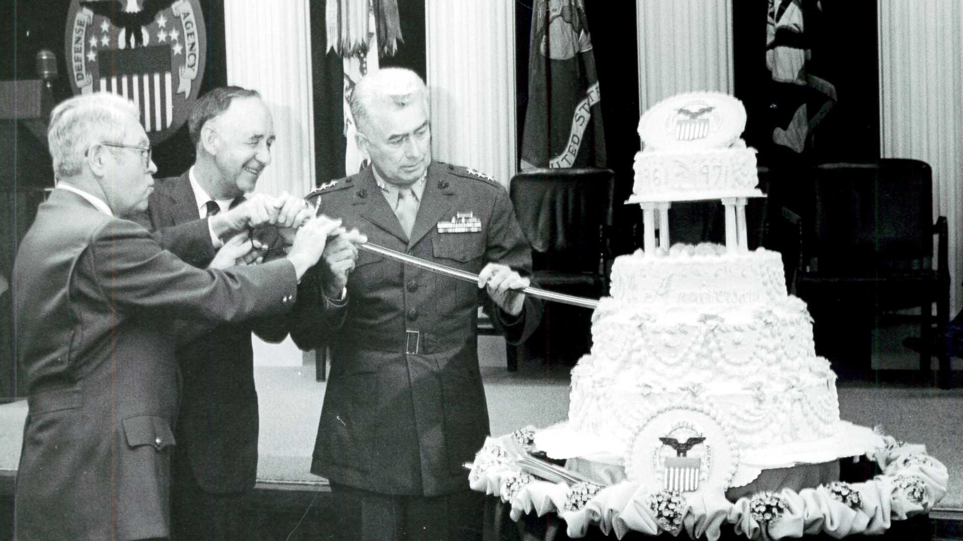 Three men use a sword to cut a cake.