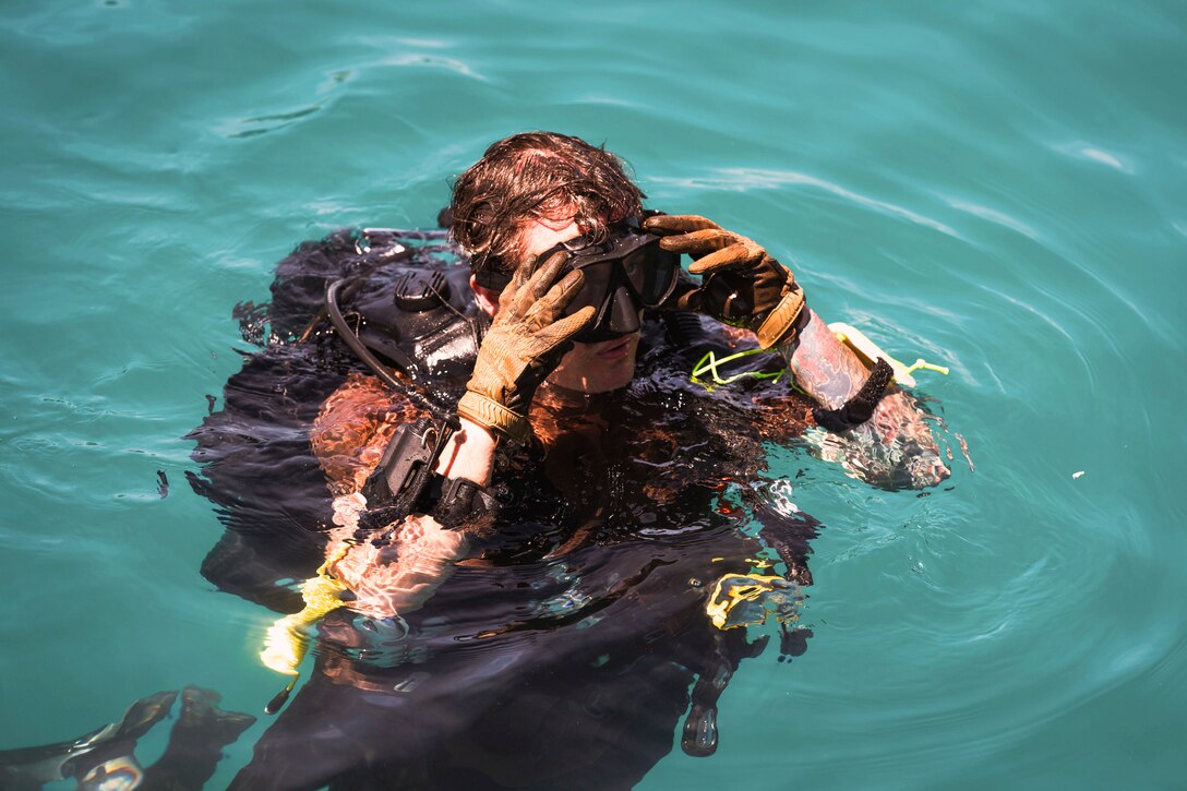 A sailor adjusts a face mask while floating in a body of water.
