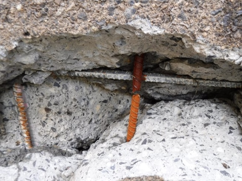 A large crack in concrete reveals broken and bent rebar.