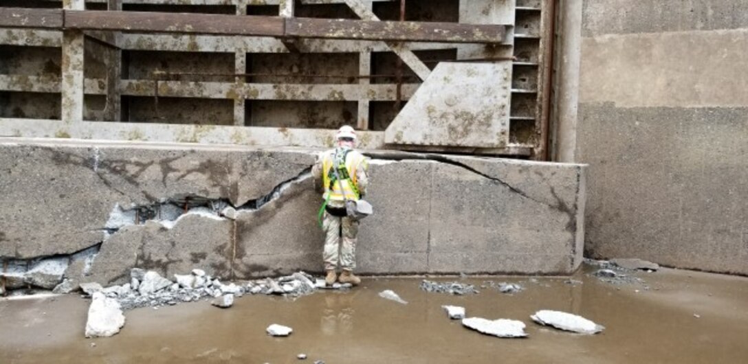 An engineer inspects a large block of concrete that has visible cracks in it.