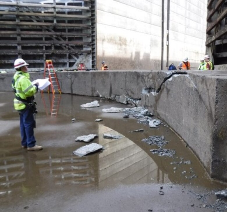 Engineers stand near a large block of concrete that has visible cracks in it.