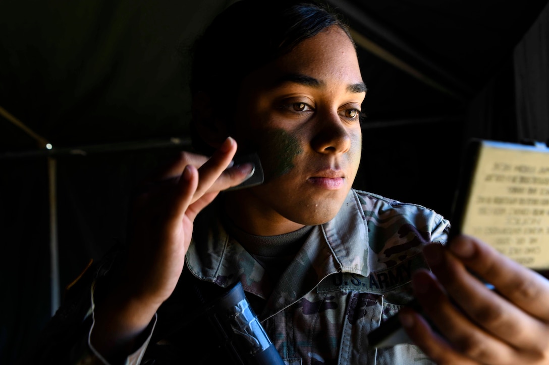 A soldier applies camouflage paint to her face.