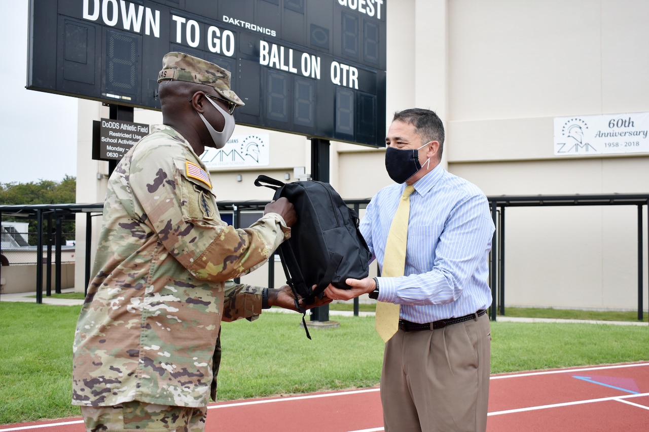 A soldier handing a school principal a backpack.