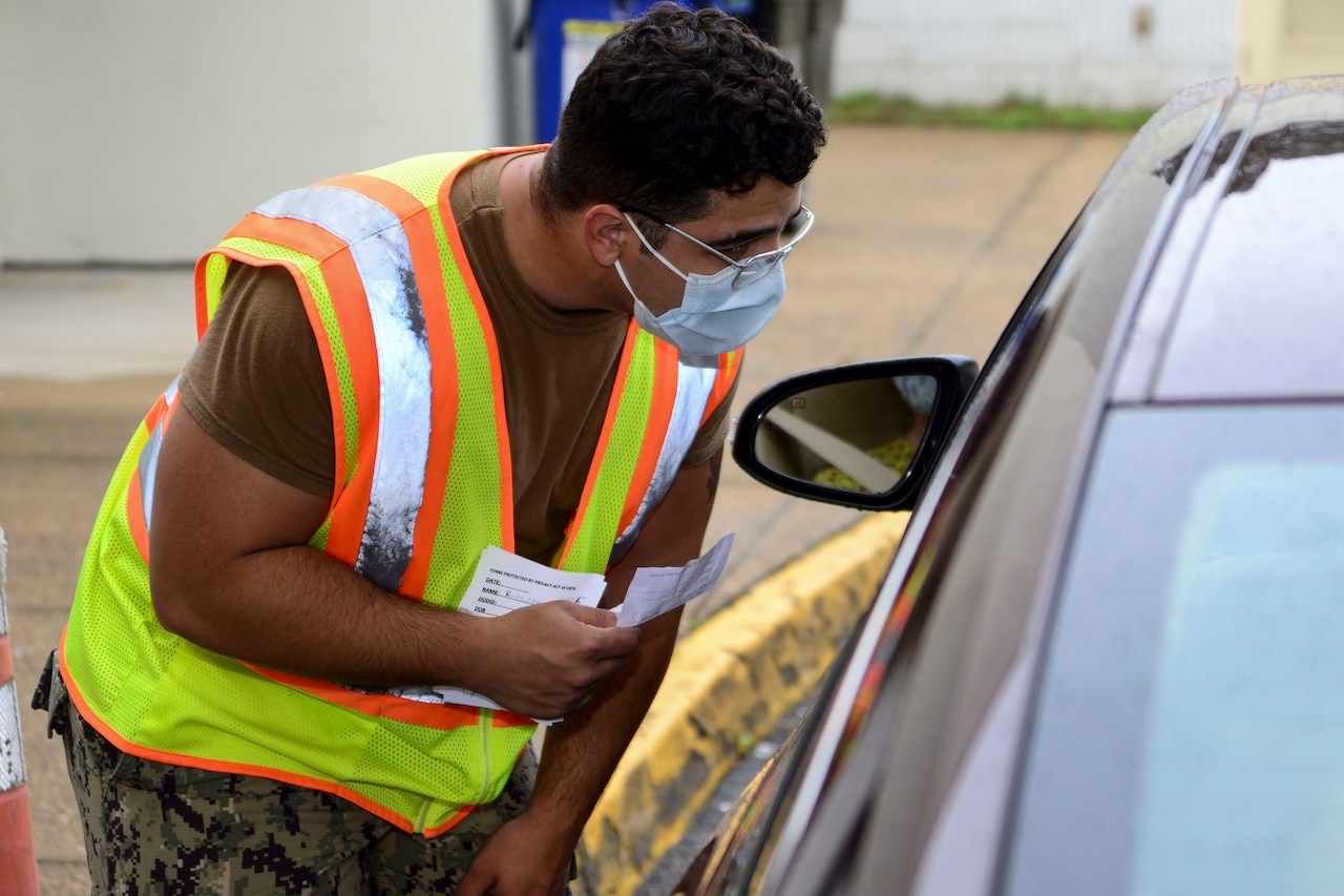 A sailor wearing a face mask verifies a patient's prescription information.