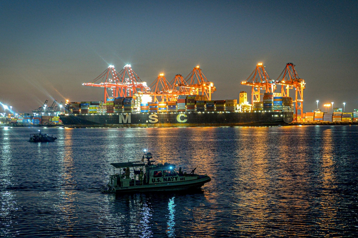 Sailors operate patrol boats surrounded by large ships.