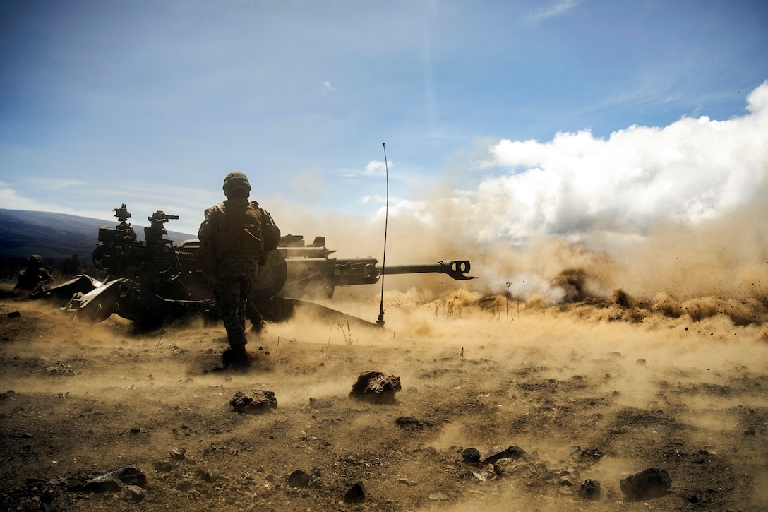 Marines fire a weapon surrounded by dust in the air.