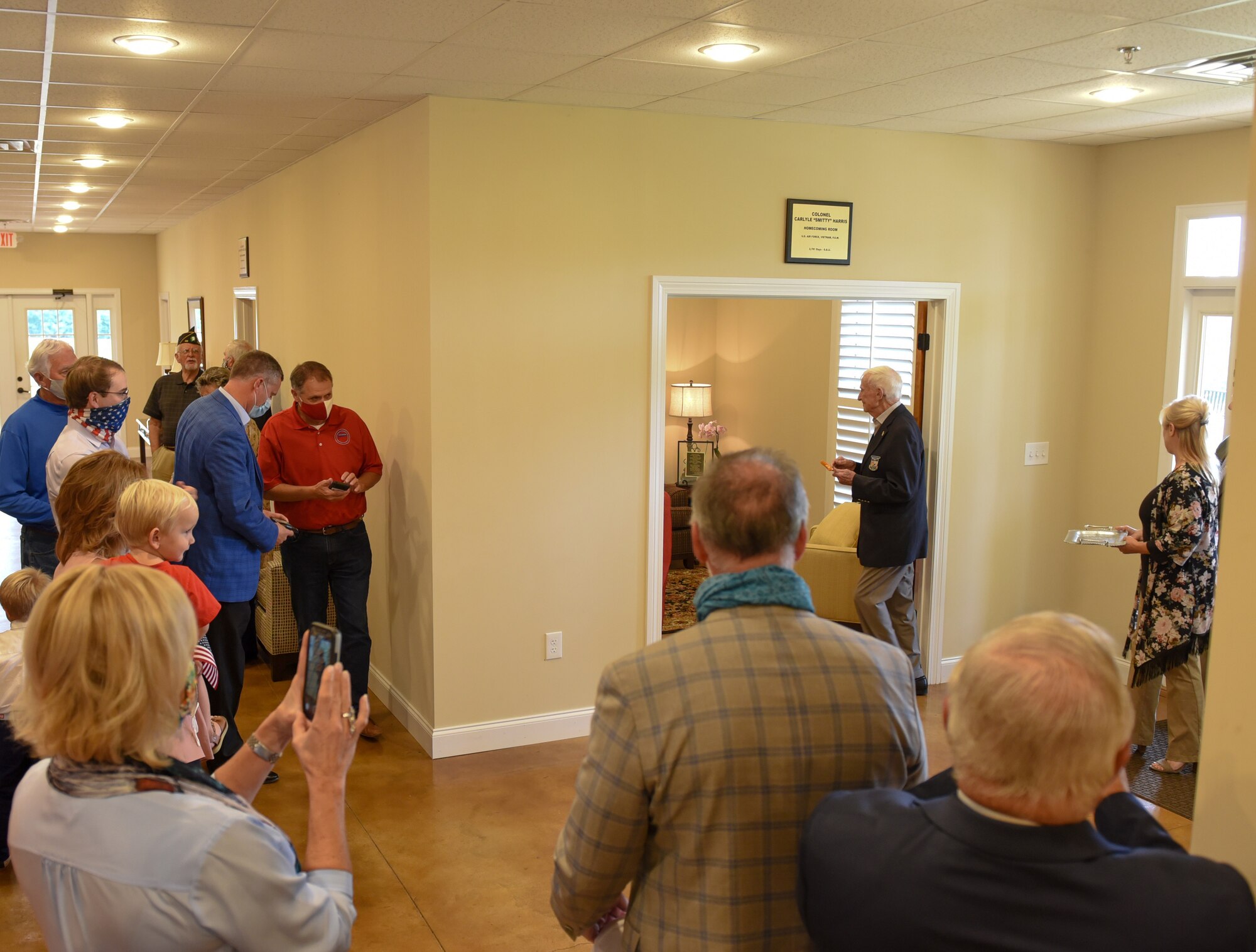 Family and friends gather around as Ret. Col. Carlyle “Smitty” Harris, former prisoner of war, cuts a ribbon and enters room dedicated to himself on September 18, 2020, in Tupelo, Miss. Prior to being caught as a prisoner of war, Harris was piloting and completing missions in the Republic F-105 Thunderchief. (U.S. Air Force photo by Airman 1st Class Davis Donaldson)