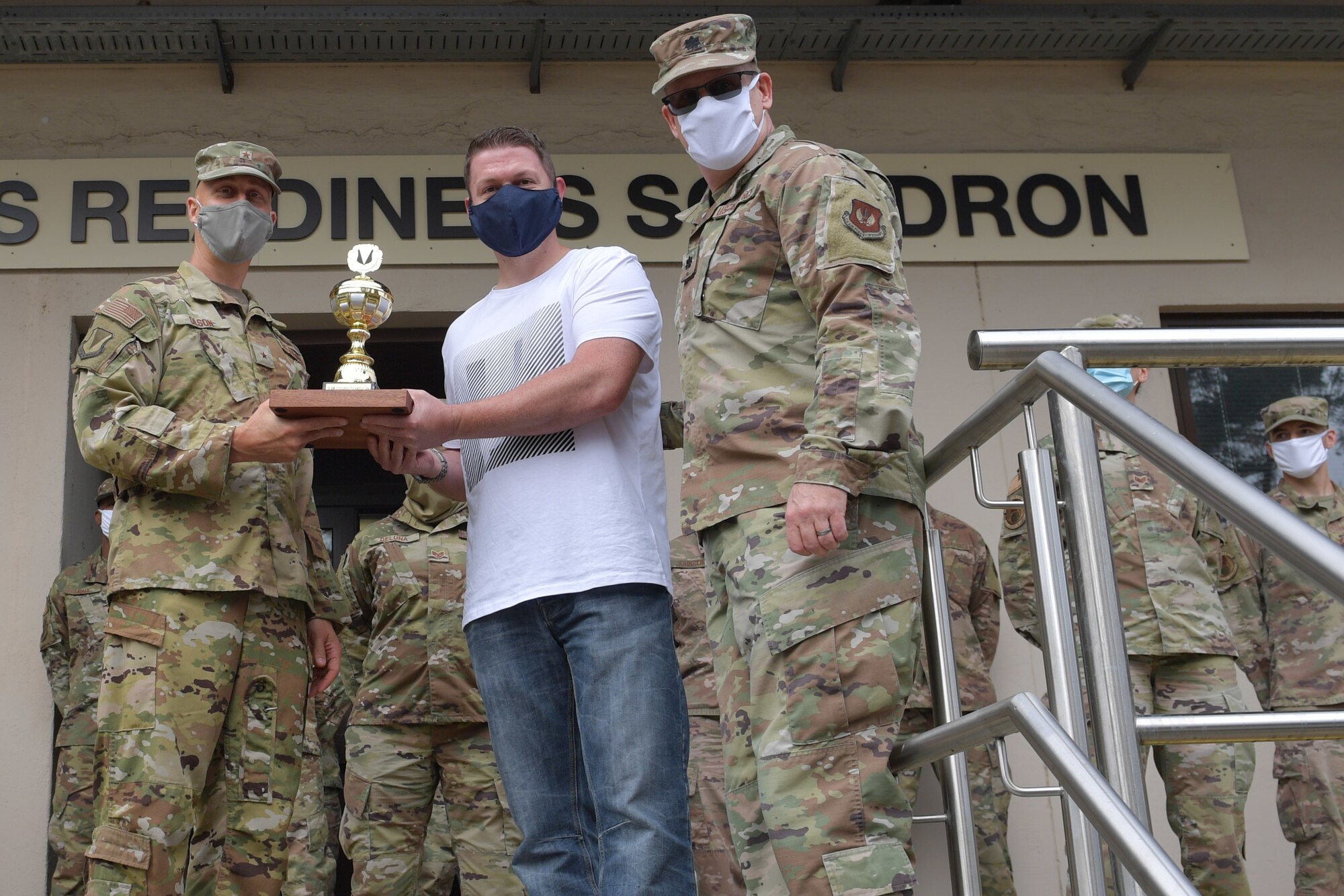 Two Airmen and a civilian posing for a photo with a trophy.