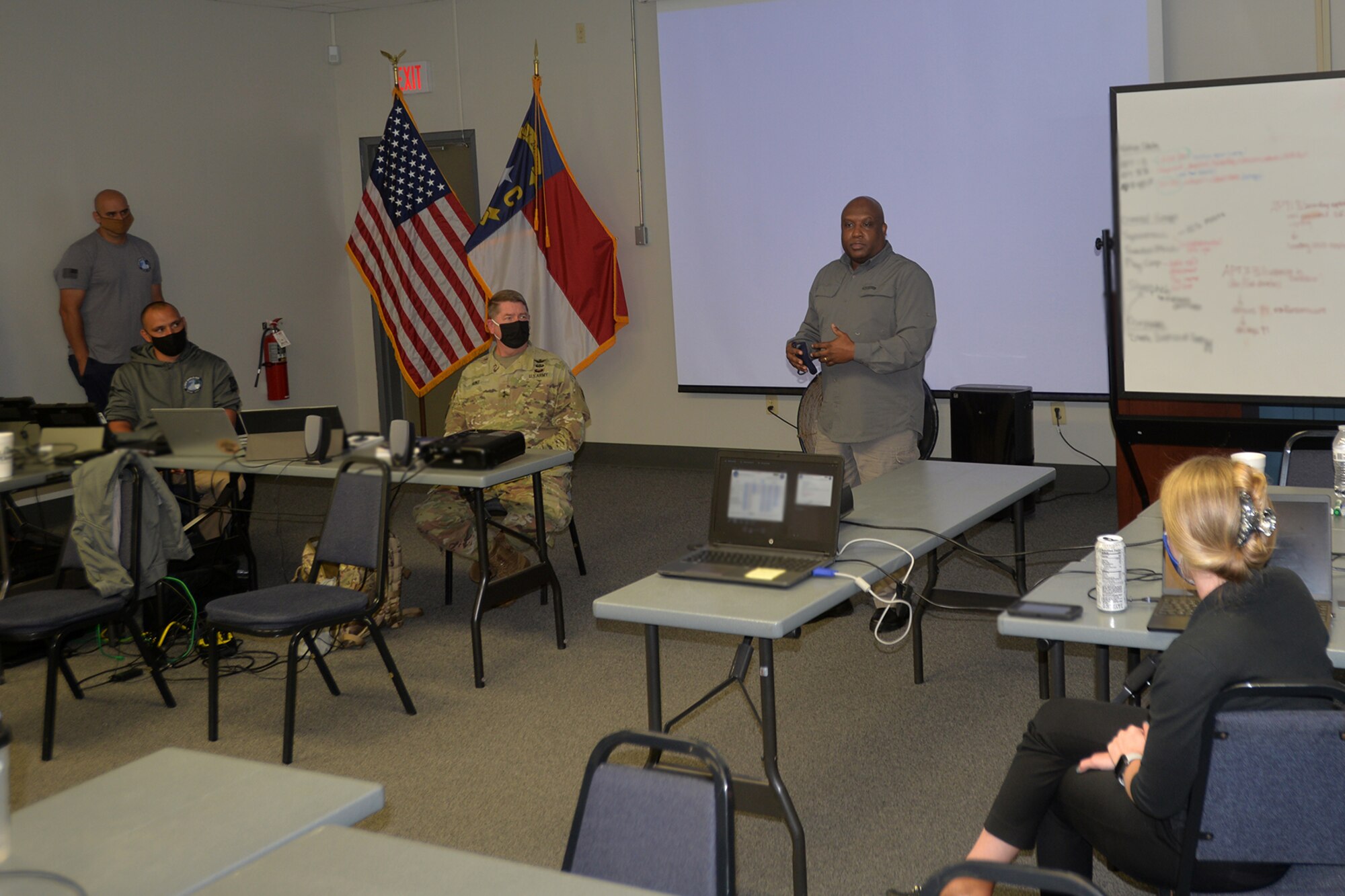 Erik A. Hooks, secretary of the North Carolina Department of Public Safety, discusses cyber operations with North Carolina National Guard (NCNG) and North Carolina State Government cyber experts during Cyber Shield 2020 held at the NCNG’s Fort Fisher Training Center, Kure Beach, North Carolina, Sept. 24, 2020.  Cyber Shield 2020 is a virtual national exercise where NCNG participants join their National Guard peers across the country, testing their response to real world cyber threats to government and private industry networks and information technology infrastructure. NCNG Adjutant General Maj. Gen. Todd Hunt, seated next to the flags, also met with the participants   (U.S. Army National Guard photo by Robert Jordan, North Carolina National Guard Public Affairs)