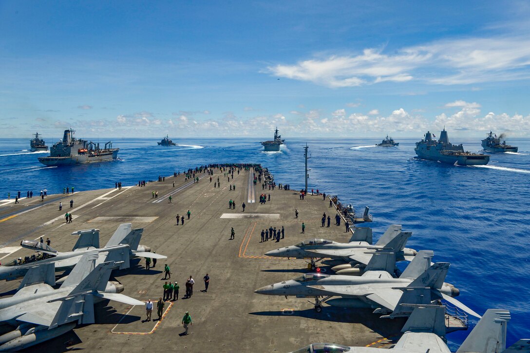 A group of military ships move through the ocean.