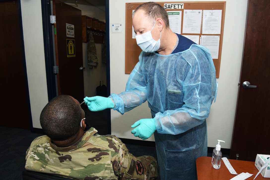 An airman wearing personal protective equipment performs a nasopharyngeal swab on another airman.