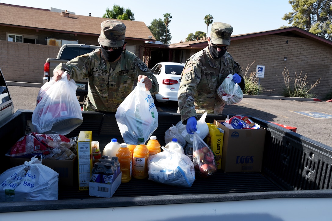 Two service members wearing face masks and gloves organize groceries in the back of a truck for delivery