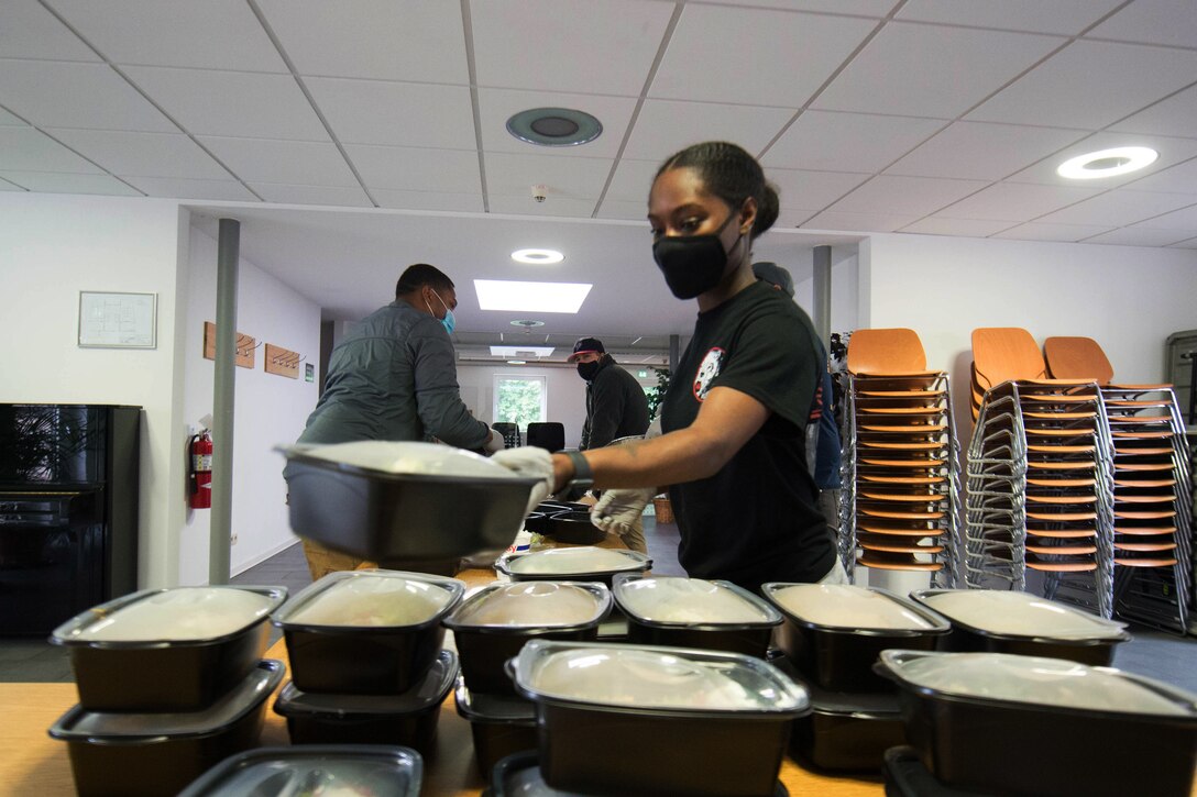 An airman wearing a face mask and gloves prepare packaged meals.