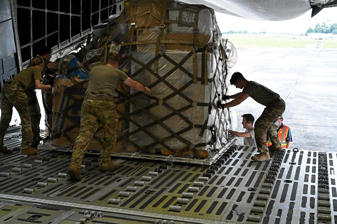 Airmen guide a pallet of supplies off of a large aircraft.