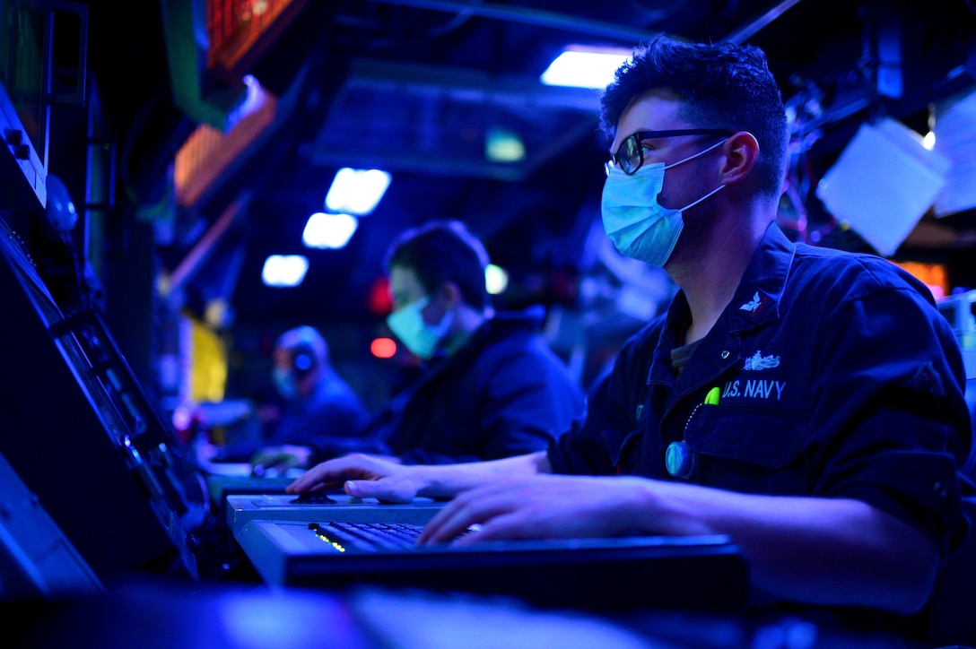 A sailor bathed in blue light sits at a console.